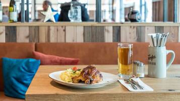 A dining table with a plate of food, a glass of beer, and a mug.