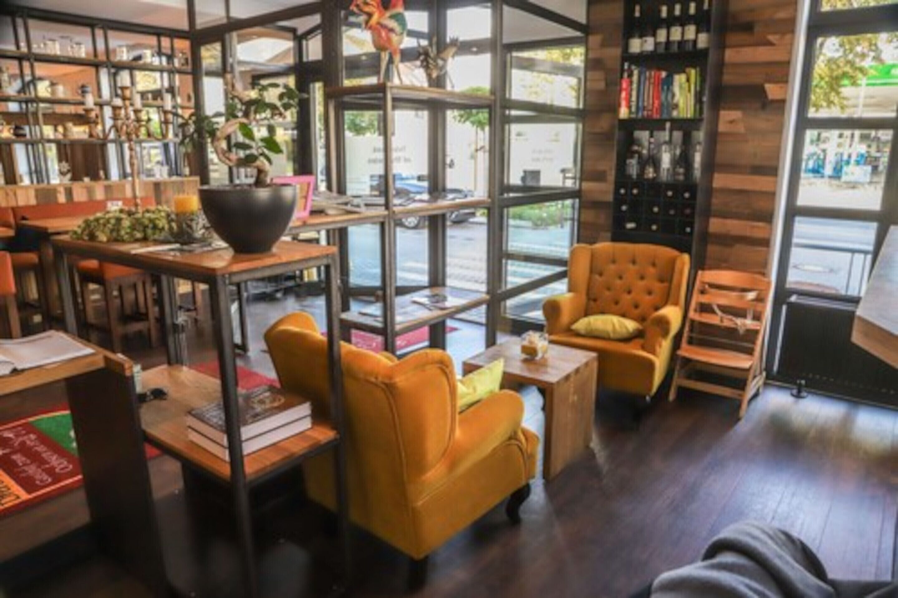 Un intérieur chaleureux avec un canapé, des fauteuils et une table basse, entouré d’étagères et d’une grande fenêtre donnant sur l’extérieur.