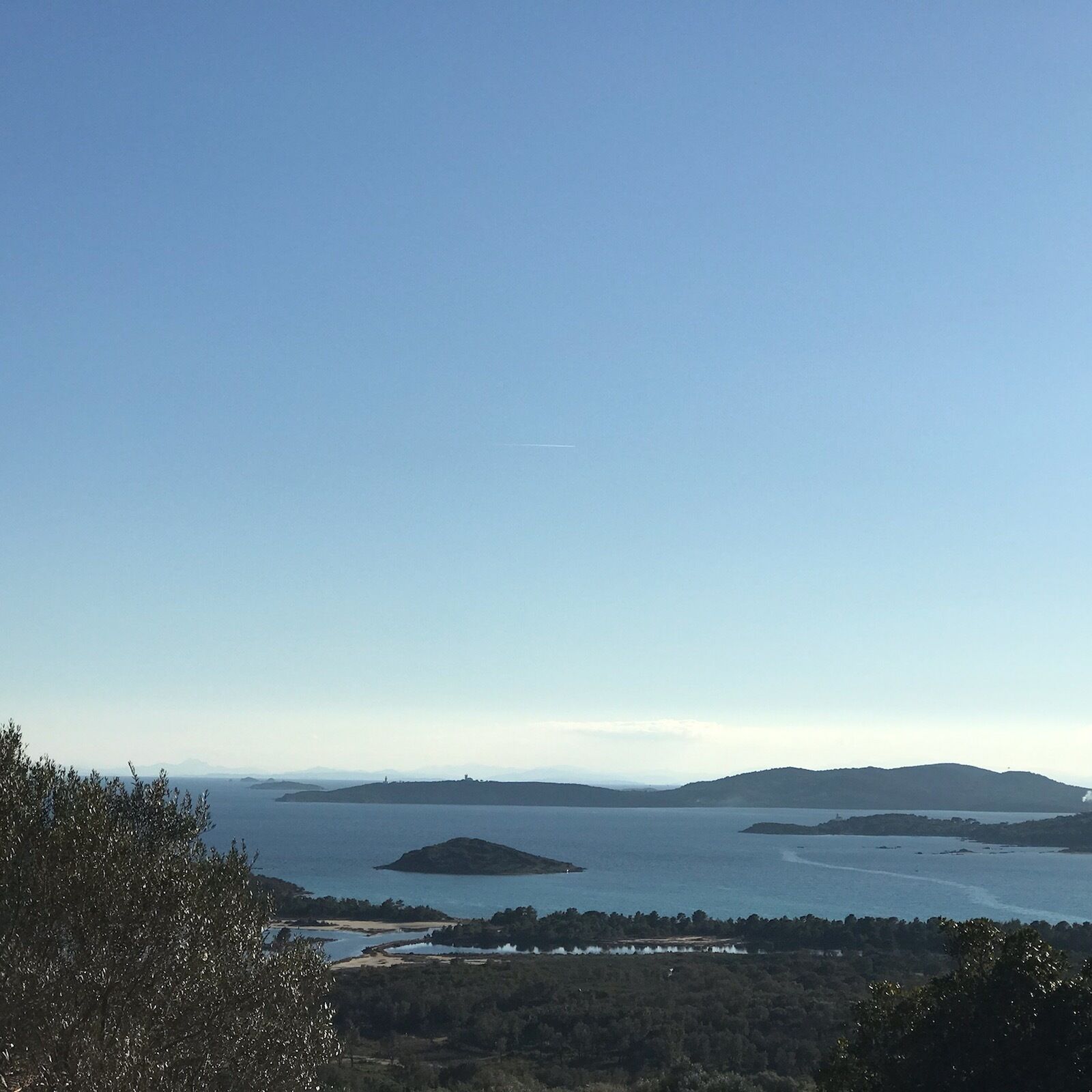 Paisaje costero con cielo despejado, islas distantes y una zona boscosa.