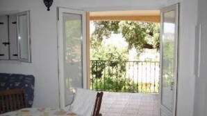 A room with a bed, a chair, a table, and a balcony with a view of trees and a fence. - houses / villas - 3 rooms - 4/5 persons (Zonza)