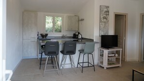 A compact kitchen with a central island, three bar stools, a television on a stand, and a door leading to another room. - houses / villas - 3 rooms - 4/5 persons (Zonza)