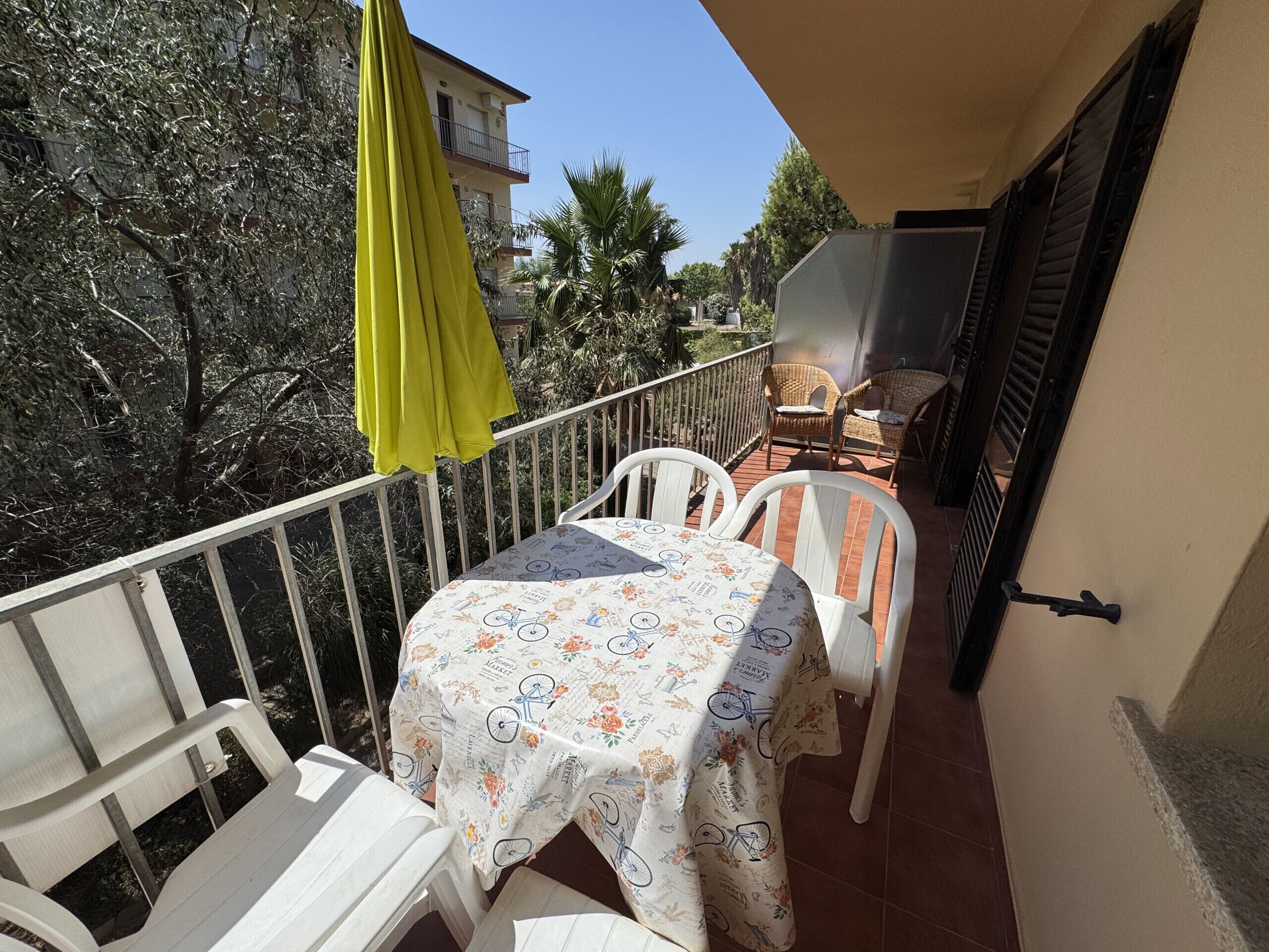 A balcony with a table and chairs, a yellow umbrella, and a view of buildings and trees.