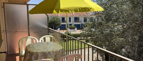 A balcony with a yellow umbrella, a table with chairs, and a view of buildings and trees.