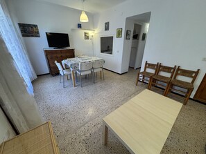 Ein Essbereich mit Tisch und Stühlen, einem Fernseher und einer Küchenzeile mit Schränken und einer Mikrowelle.