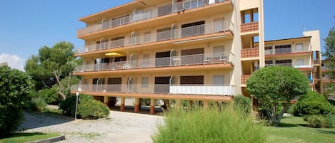 A multi-story hotel with balconies, a covered outdoor seating area, and a landscaped garden.