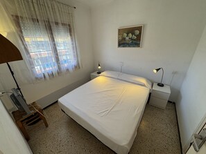 A bedroom with a bed, two bedside tables, a lamp, a chair, a window with curtains, and a painting on the wall.