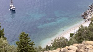Un paysage côtier avec un bateau ancré près d’une plage, entouré d’une eau claire et d’une côte rocheuse.