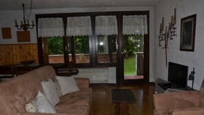 Una sala de estar con un sofá marrón, una mesa de centro, un televisor y una ventana con cortinas de encaje.