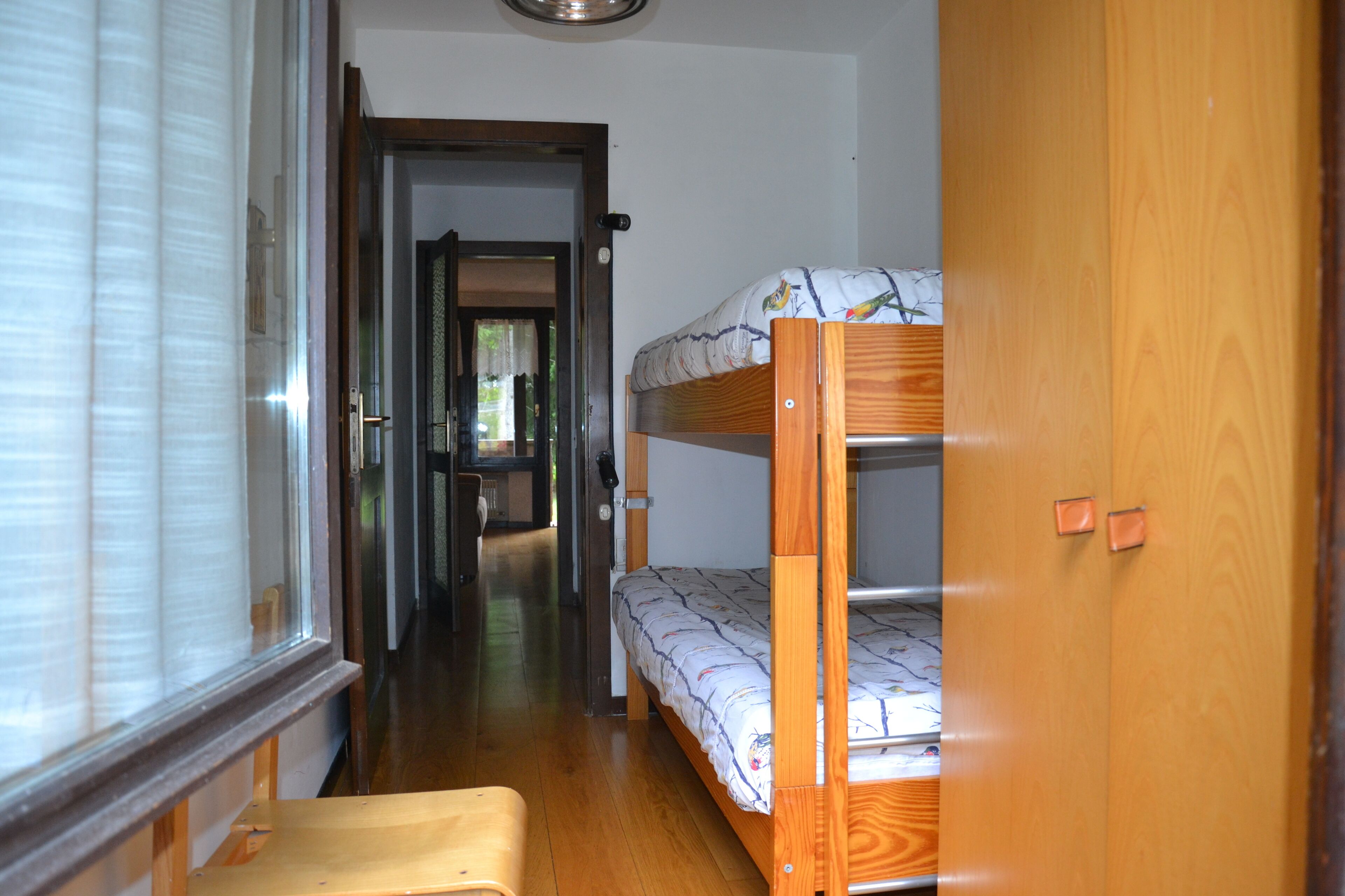 A narrow hallway with a bunk bed, a wooden door, and a window with blinds.
