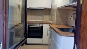 Una cocina compacta con gabinetes blancos, horno integrado, microondas y pileta.