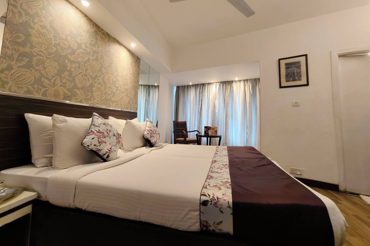 Una habitación de hotel con una cama grande, un ventilador de techo, una mesita de noche, una silla y un cuadro en la pared.