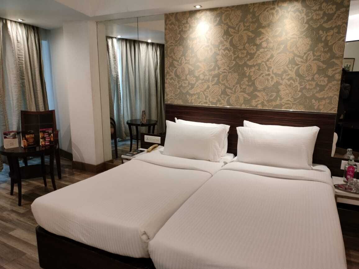 Una cama doble con sábanas blancas, cabecera de madera y pared con estampado floral.