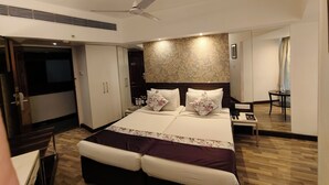A modern hotel room with a large bed, a ceiling fan, a small table, and a desk. - Regenta Place Bangalore, Cunningham Road (Bengaluru)