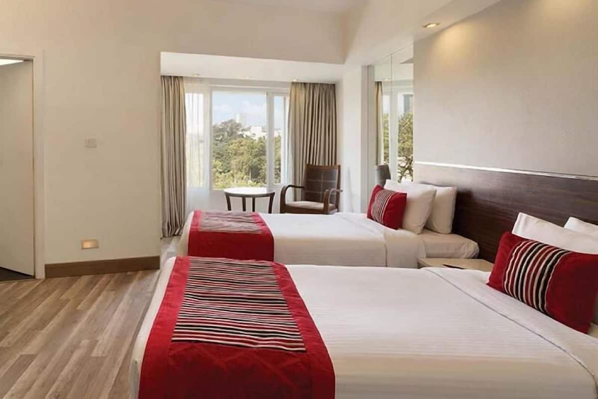 Habitación de hotel con dos camas, una mesita pequeña y una silla.