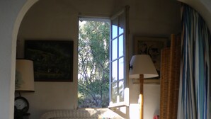 Ein gemütliches Zimmer mit einem Rattan-Sofa, einer Lampe und Blick auf Bäume durch ein Fenster.