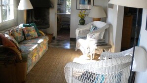 Ein gemütliches Wohnzimmer mit einer Couch, zwei Korbstühlen, einem Kamin und einem Bücherregal.