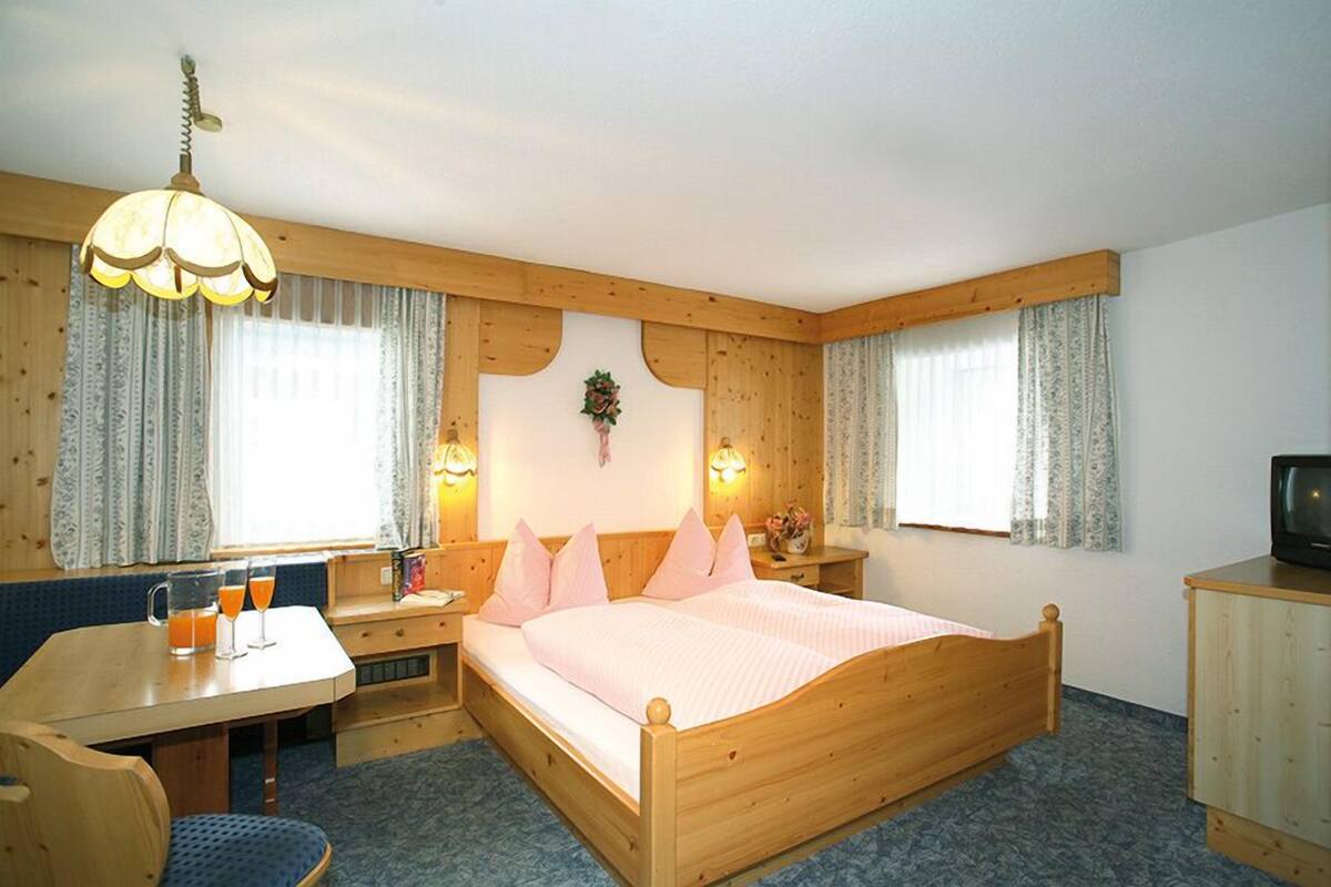Una habitación acogedora con una cama de madera, un escritorio con silla, un televisor y dos ventanas con cortinas.