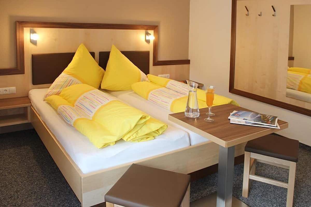 Una habitación de hotel con una cama, mesitas de noche, un espejo y un banco.