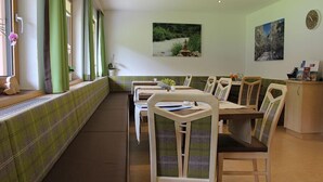 Un espace repas comprenant un long banc, des chaises et une table agrémentée d’un vase de fleurs.