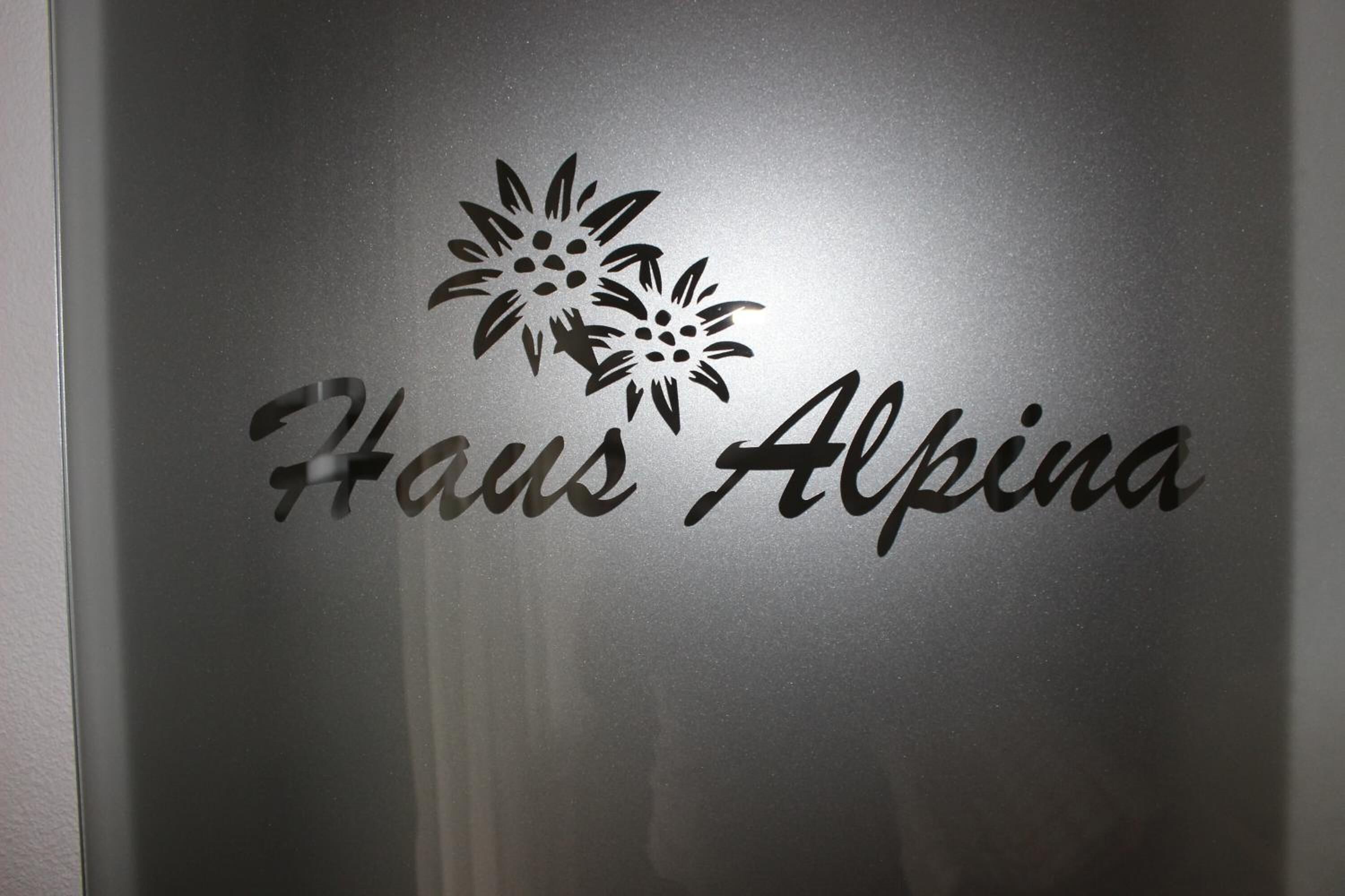 A logo with the text "Haus Alpena" and floral designs.