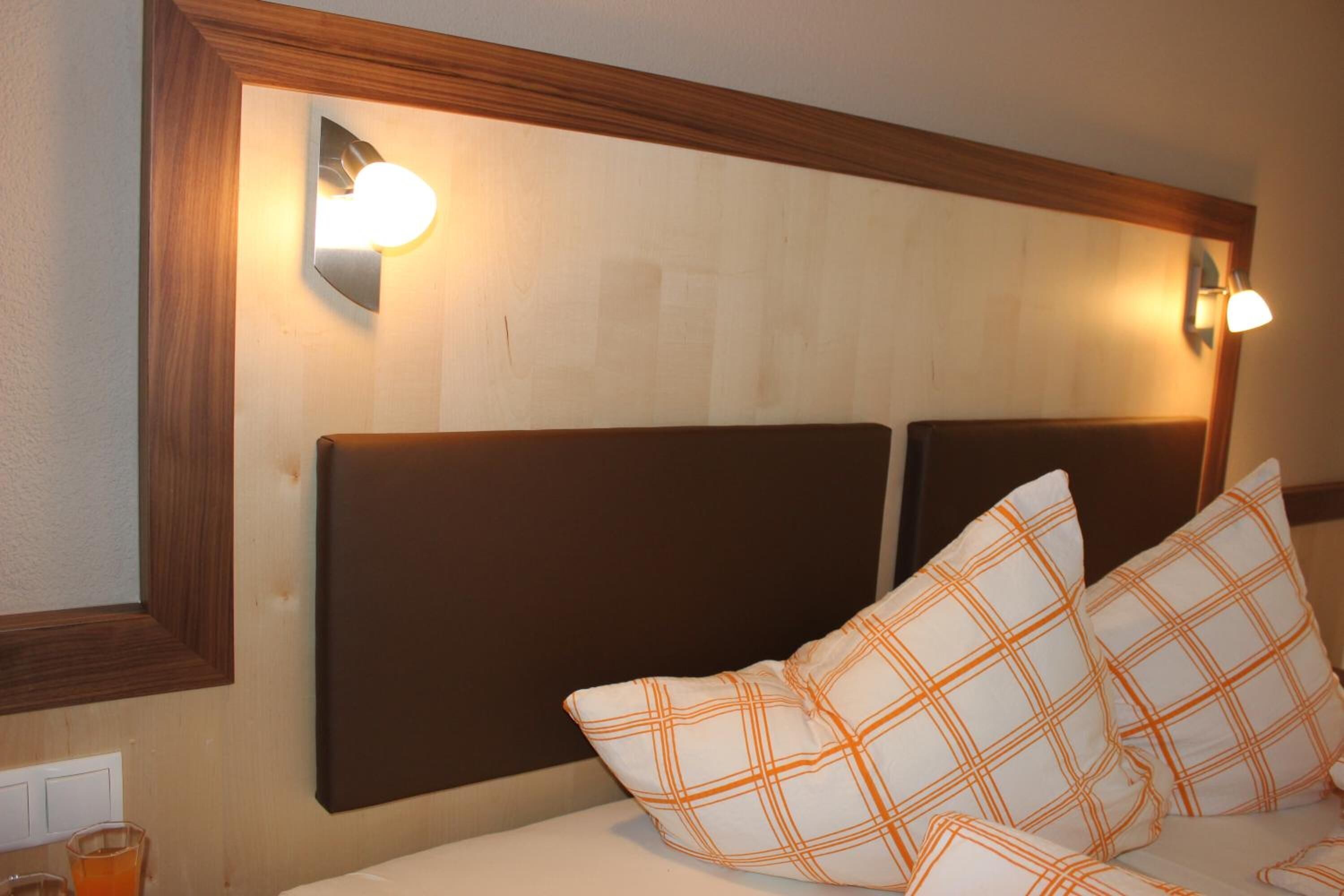 A hotel room with a wooden headboard, two wall-mounted lights, and a bed with white bedding and orange plaid pillows.