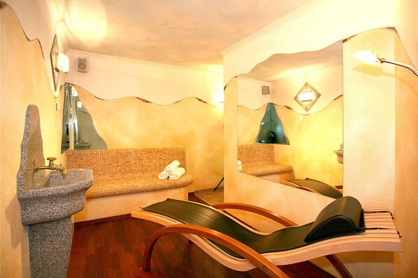 Un cuarto de spa con un lavamanos de piedra, dos sillones acolchados, un espejo y una toalla pequeña en el banco.