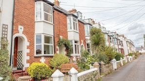 A row of terraced houses with brick facades, white window frames, and a variety of plants and shrubs in the front gardens. - House, Attractive Views Of The Byes, Family and Pet Friendly (Sidmouth)