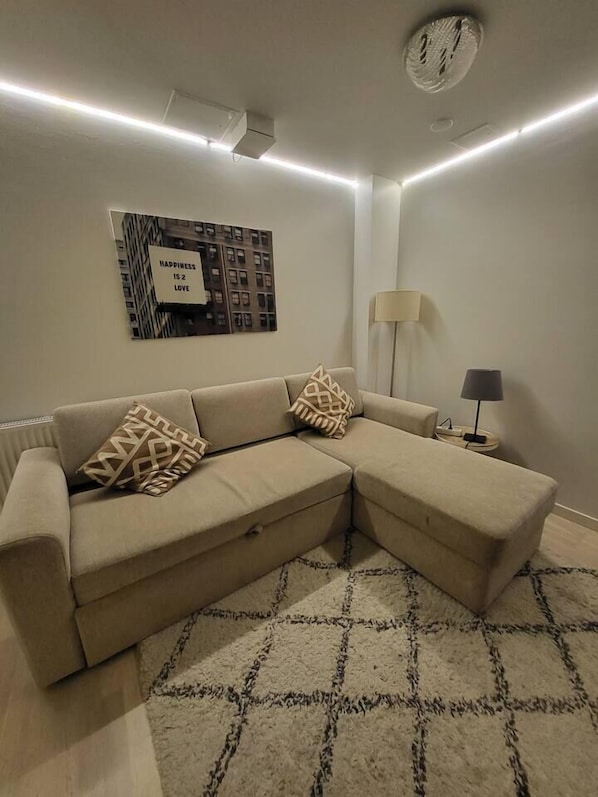 A beige sectional sofa with patterned cushions, a floor lamp, and a wall-mounted artwork with the text 'HAPPINESS IS LOVE.'