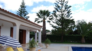 A poolside area with lounge chairs, a striped umbrella, and potted plants. - Modern Villa in a quiet spot, with a large private  swimming pool (Espiche  Luz Lagos)