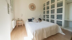 A bedroom with a bed, a bedside table, a wall-mounted light, a radiator, and a wardrobe with glass doors.