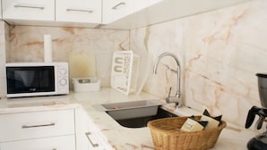 A modern kitchen with white cabinets, a built-in microwave, a sink with a faucet, and a marble backsplash. - Cozy Apartment in Anjos | Maria da Fonte | Terrace (Lisboa)