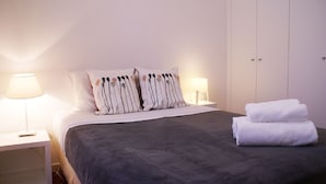 A bedroom with a bed, two bedside lamps, a nightstand, a wardrobe, and a set of towels. - Cozy Apartment in Anjos | Maria da Fonte | Terrace (Lisboa)