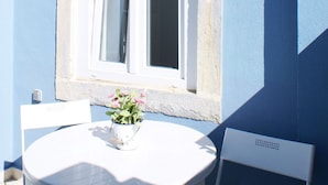 A small outdoor seating area with a round table and a chair, a window with a white frame, and two wall-mounted light fixtures. - Cozy Apartment in Anjos | Maria da Fonte | Terrace (Lisboa)