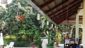 A covered outdoor area with a patio, potted plants, a dining table, and outdoor furniture. - Longan Tree (Saraphi)