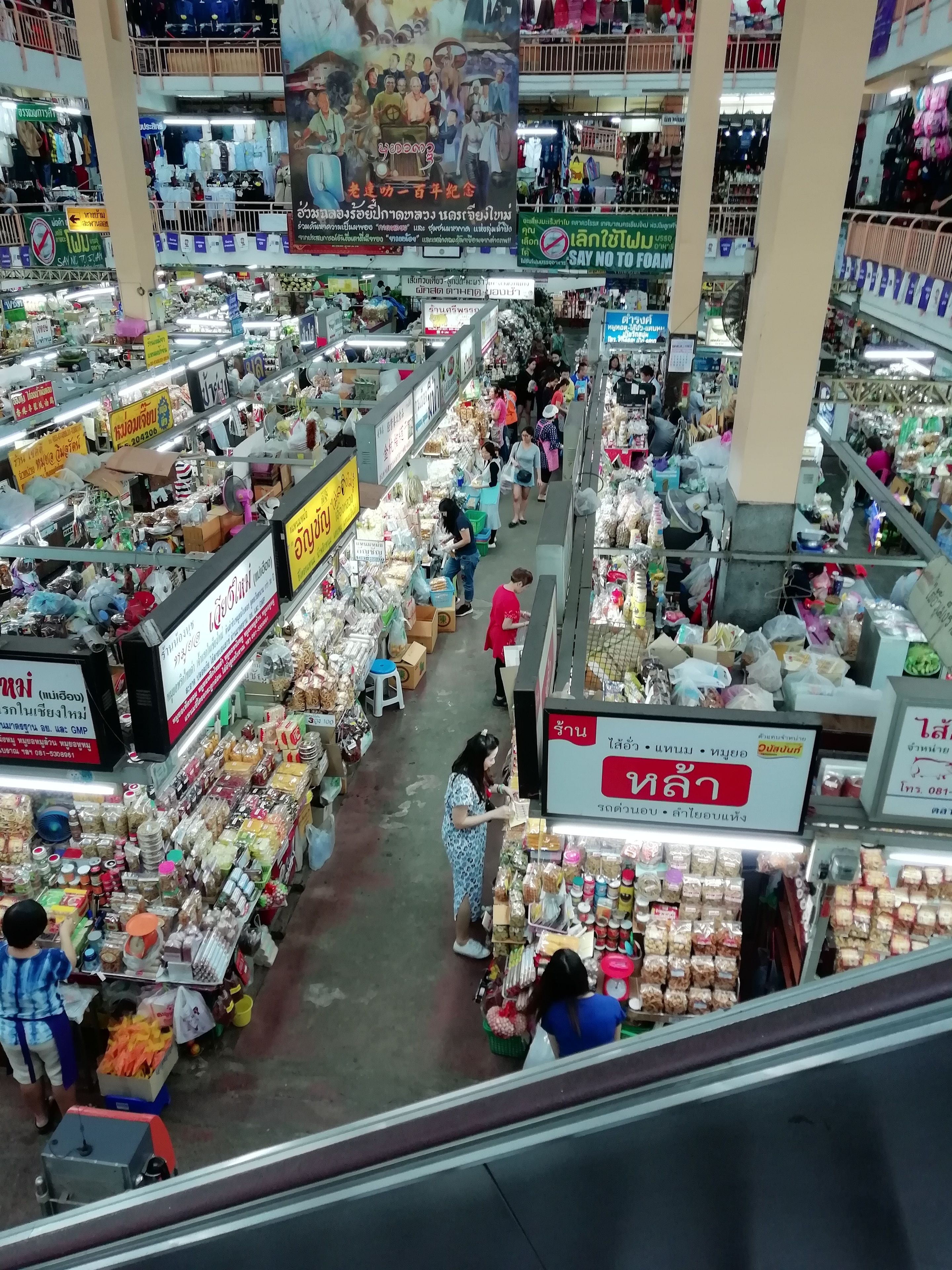 A busy indoor market with various stalls selling food, household items, and clothing.
