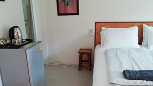 A hotel room with a bed, a small table, a refrigerator, a kettle, and a trash bin. - Longan Tree (Saraphi)