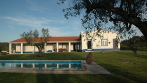 Una casa de dos pisos con piscina, un árbol grande en el jardín delantero y un cielo despejado.