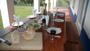 Una mesa de comedor lista para una comida, con una botella de vino, pan y una ensalada sobre una mesa de madera con vistas al campo.