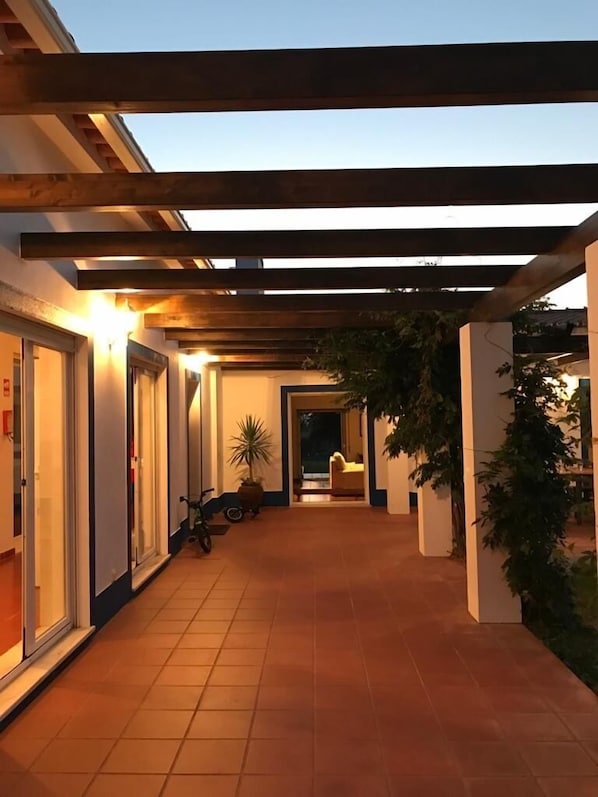 A covered corridor with tiled flooring, wooden beams, and potted plants.