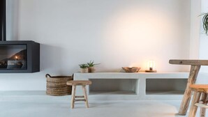 Um quarto aconchegante com lareira, um banco, um banquinho e uma mesa.