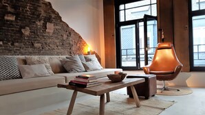 Uma sala de estar moderna com parede de tijolos, um sofá branco, uma mesa de centro de madeira e uma poltrona de couro.