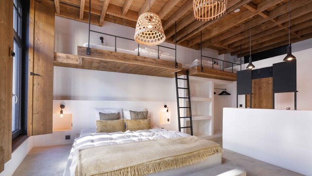 Quarto moderno com cama grande, vigas de madeira e um mezanino.