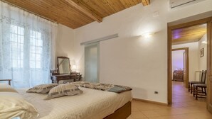 Un dormitorio con cama, mesita de noche, espejo y una puerta que da a un pasillo.