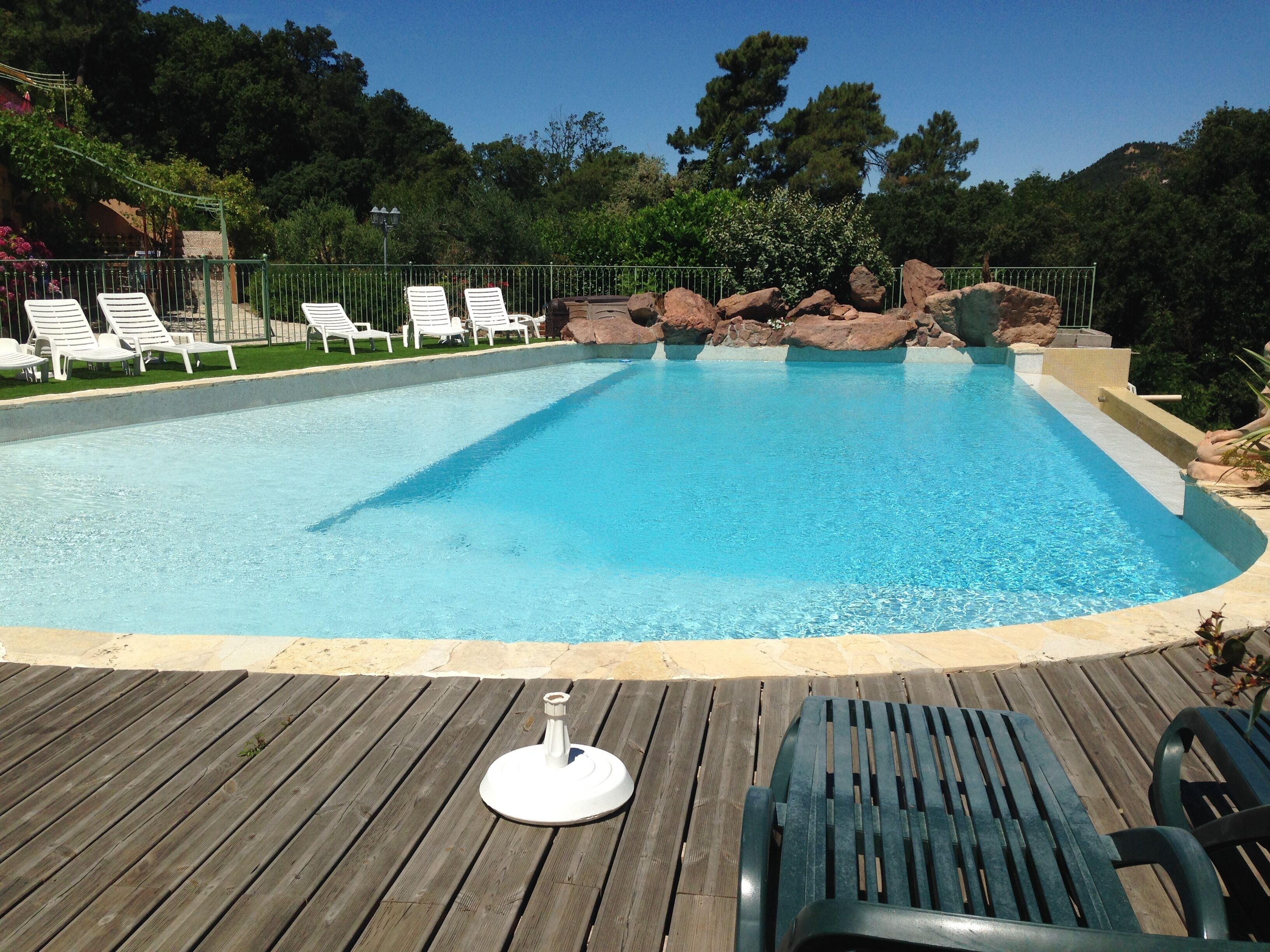 Una piscina azul cristalina con un deck de madera, rodeada de sillones blancos y una formación rocosa.
