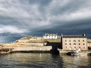 Un bâtiment situé sur la côte, avec un pont enjambant une étendue d’eau, un bateau amarré à proximité et un ciel orageux.