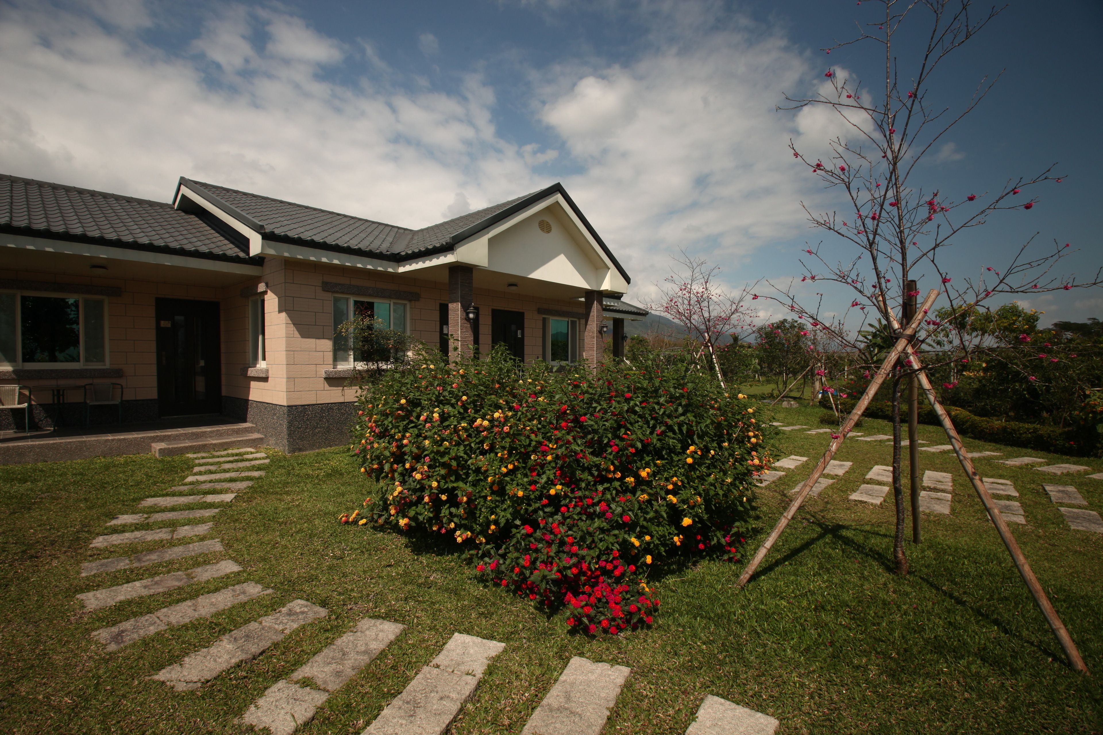 Una casa moderna con techo de tejas, un porche delantero y un jardín bien cuidado con flores coloridas.