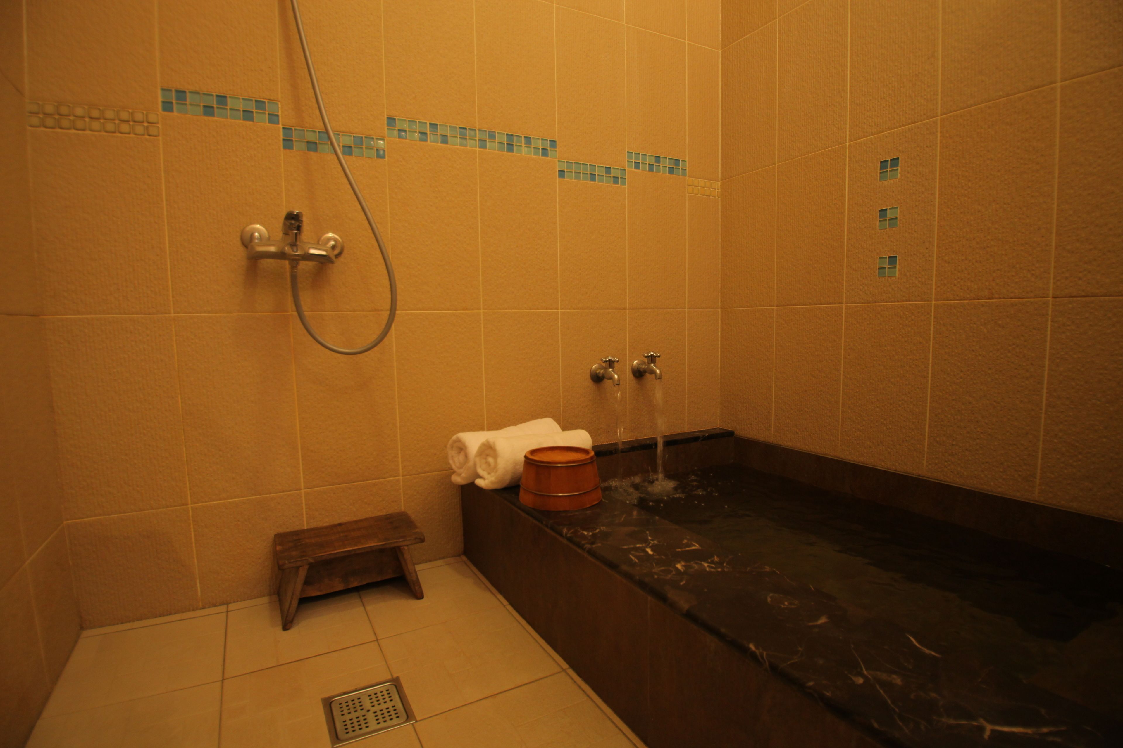 A bathroom with a bathtub, a showerhead, and a small wooden stool.