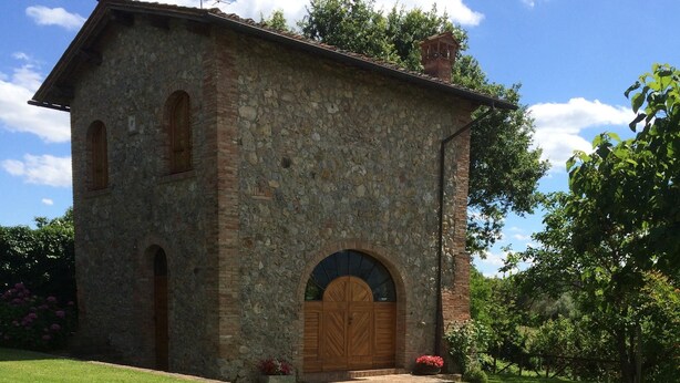 A stone building with a wooden door and arched windows, surrounded by a well-maintained garden with flowering plants.