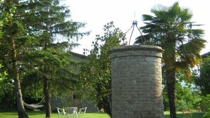 A stone structure with a satellite dish, surrounded by trees and a grassy area with a white table and chairs.
