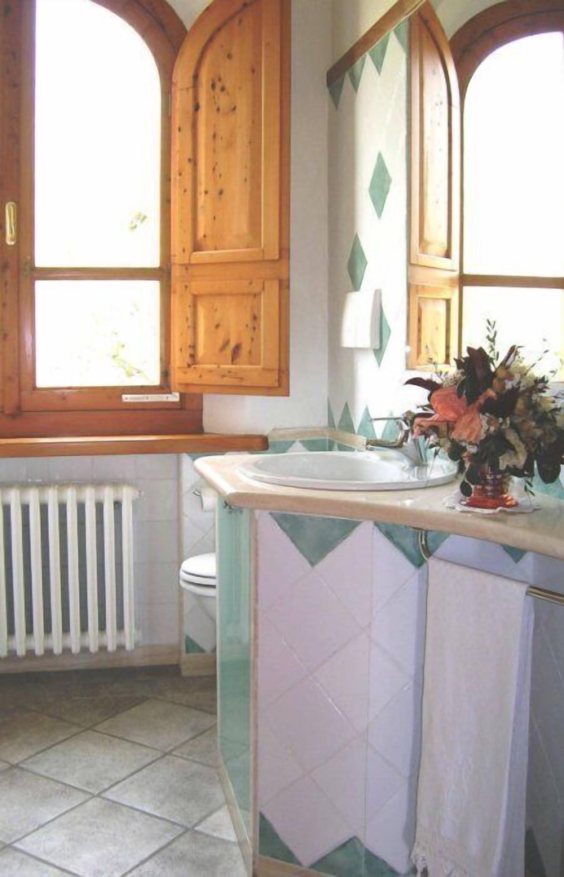 Ein Badezimmer mit Waschbecken, Holzschränken, einem Fenster und einer Heizung.
